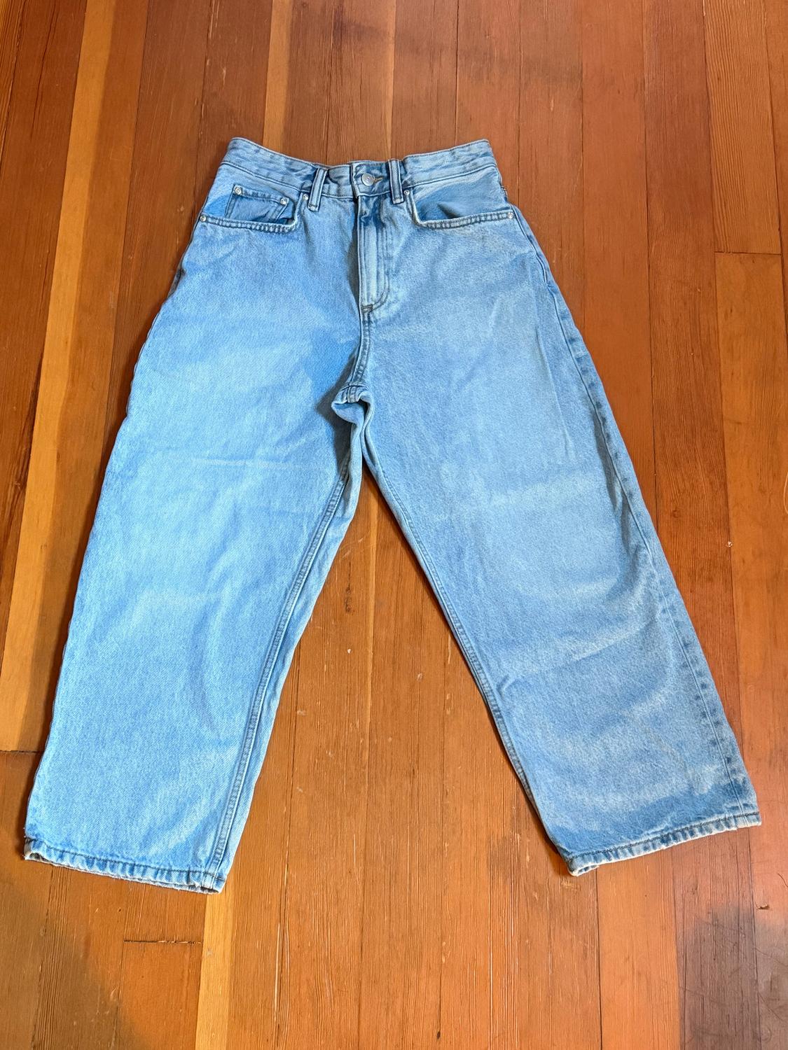 Blue, wide-leg jeans laid out on a wooden floor. The garment features a classic design with front and back pockets.