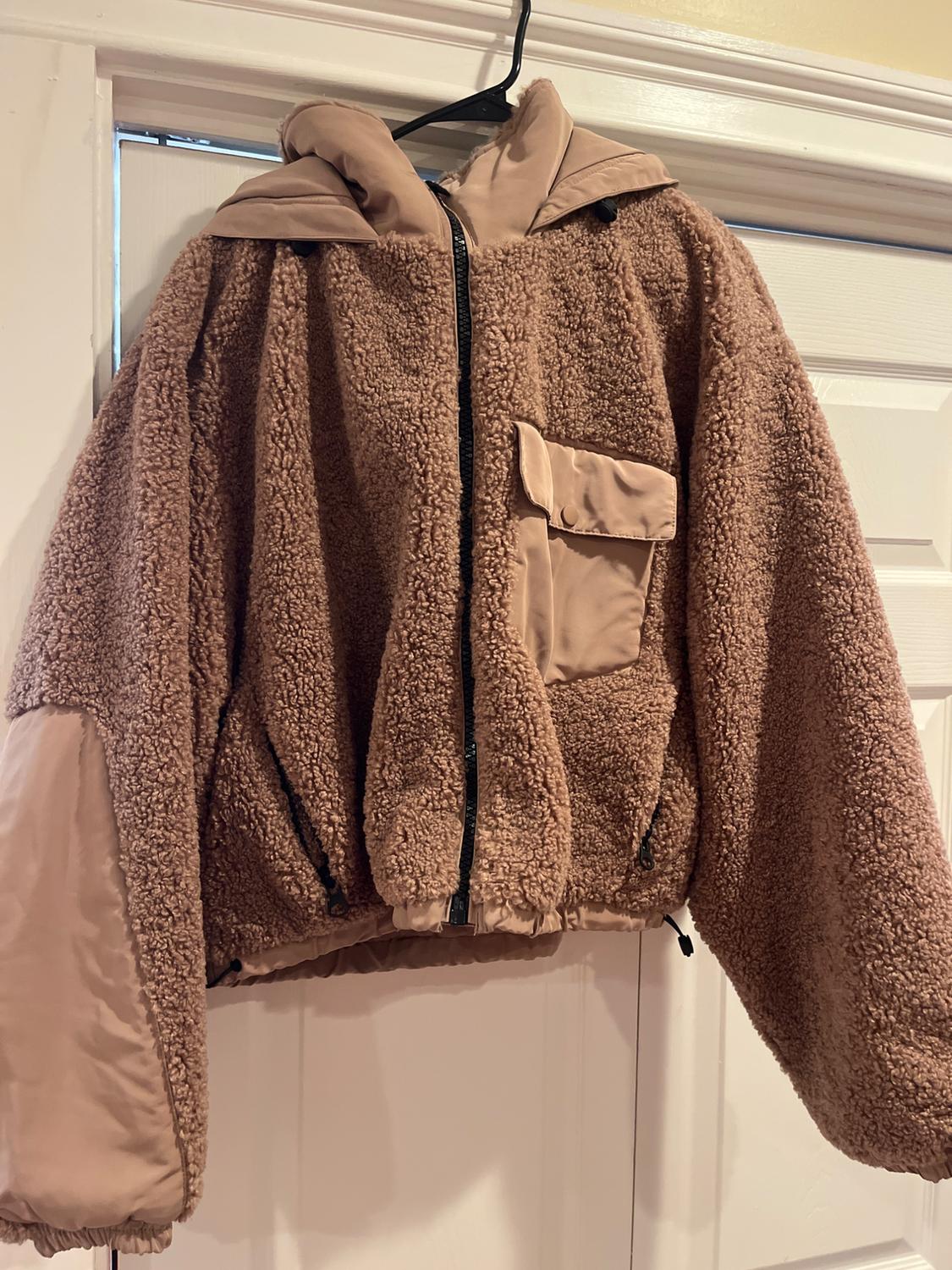 Brown wool jacket with a hood and black zip, hanging on a white door. Front pocket and plain fabric details.