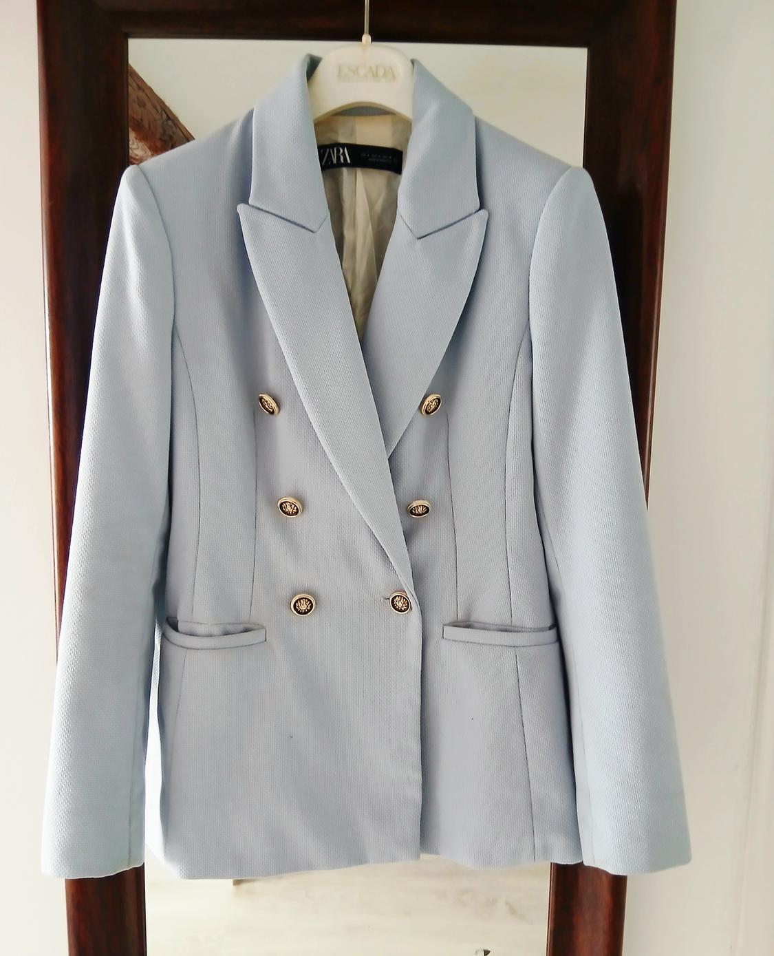 Light blue double-breasted jacket with gold buttons, hanging on a white hanger with the brand visible in the mirror.