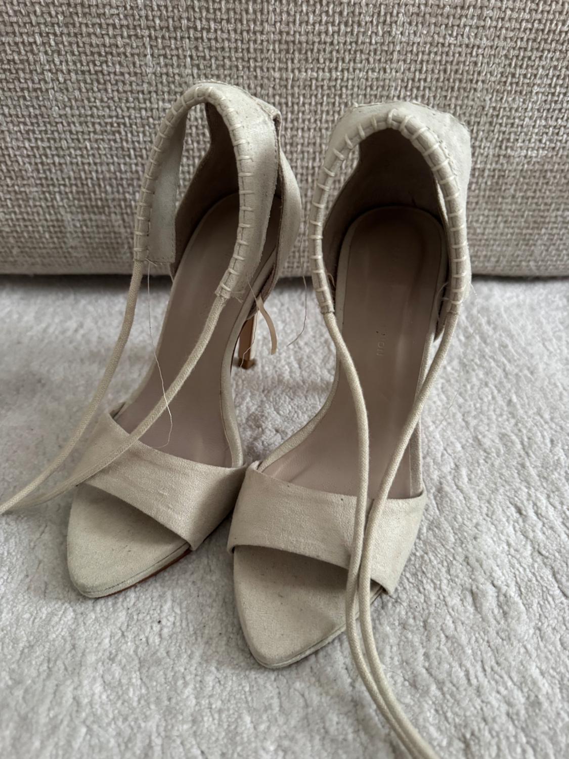 Beige heeled sandals with long straps on a light textile surface, textured fabric background.