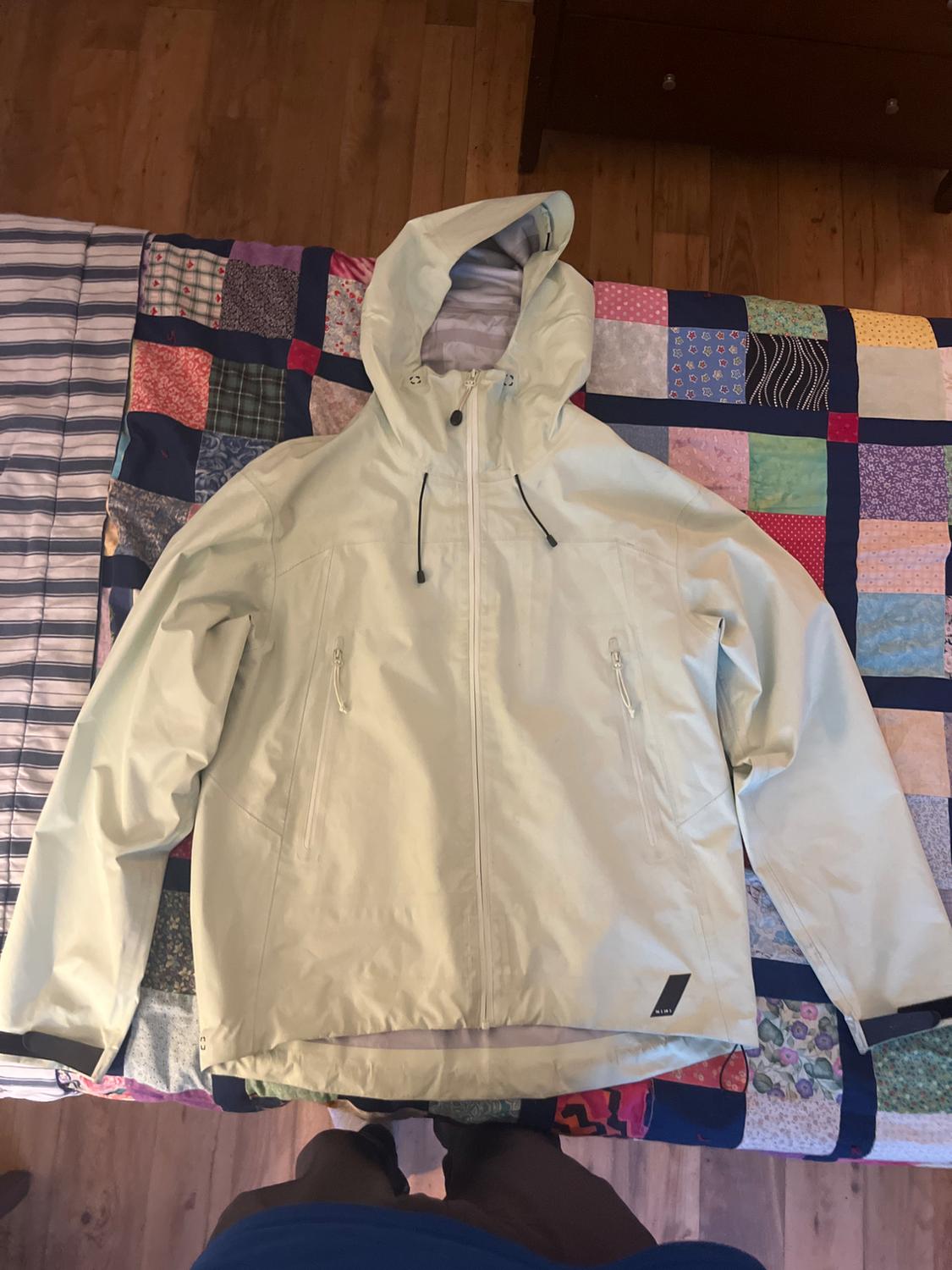 Beige hooded jacket with a front zip fastening on a colourful patchwork quilt on a wooden bed.