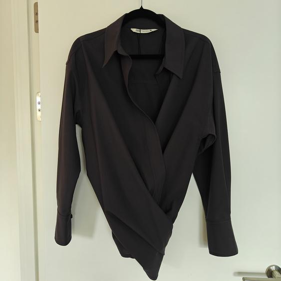 Black long-sleeved shirt hanging on a black hanger over a white door. Crossover design with a classic collar.