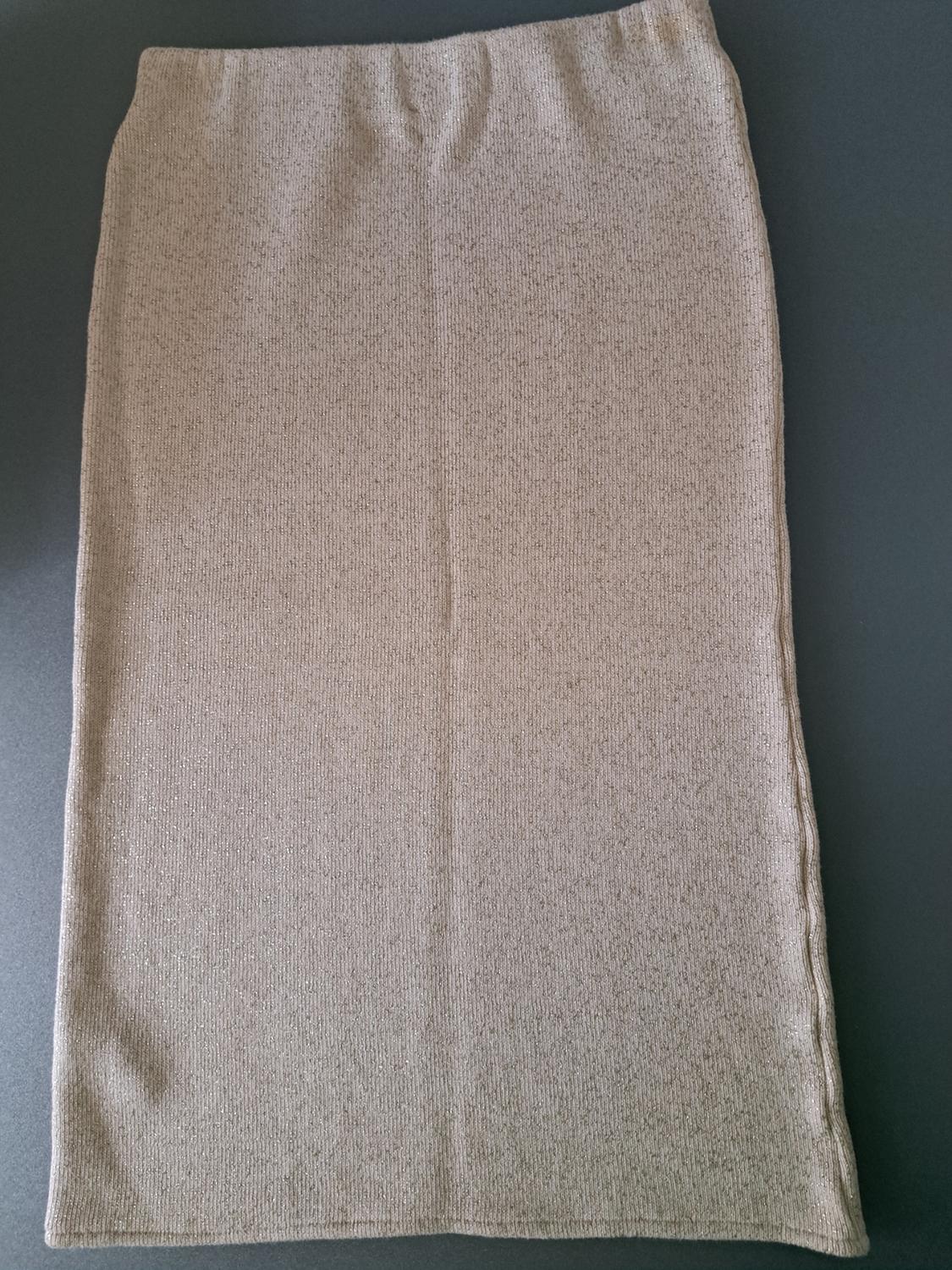 Light beige knitted pencil skirt, on a dark grey background. The texture is visible with a slight sheen.