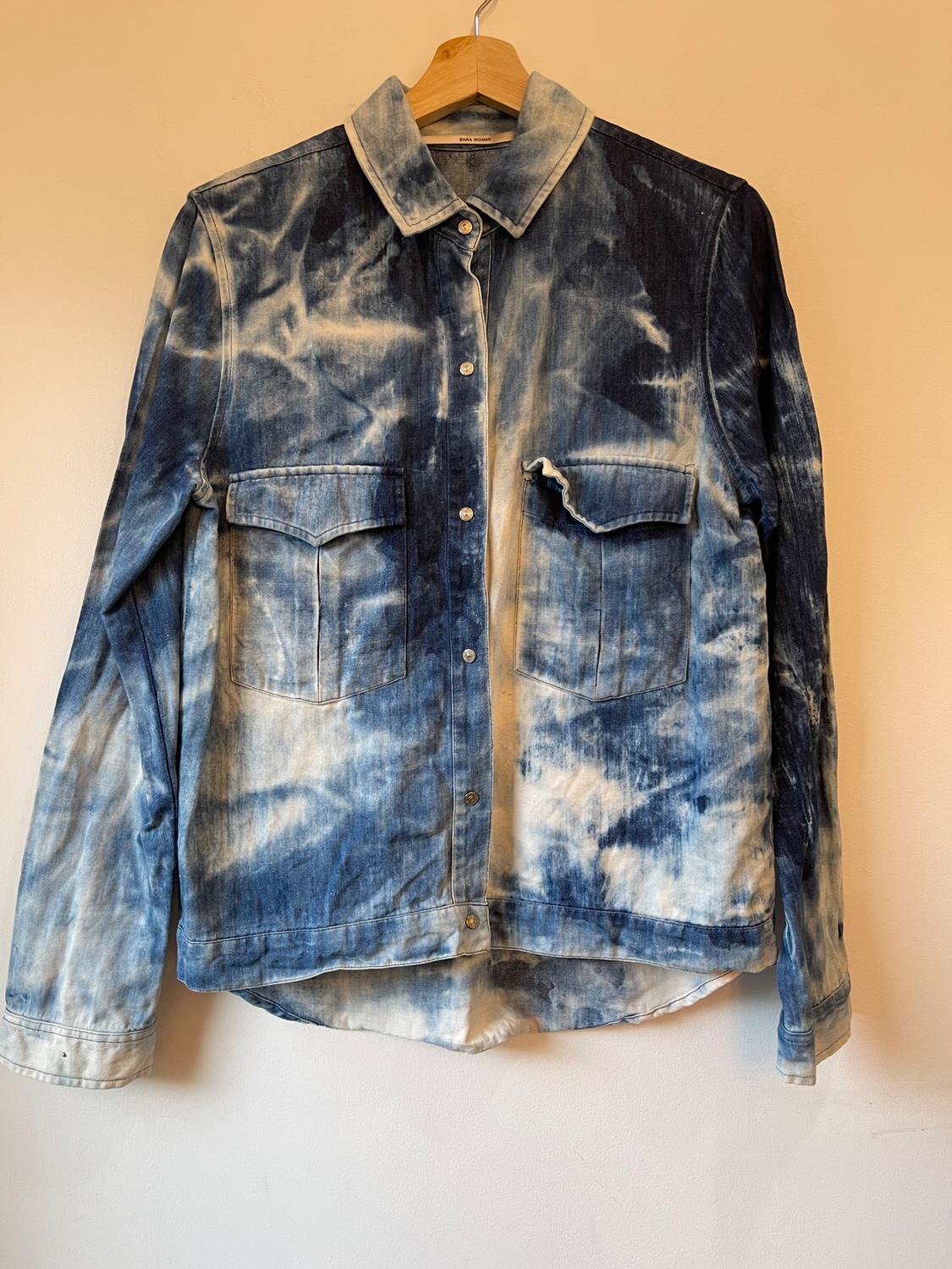 Blue and white faded denim jacket, hanging on a wooden hanger against a beige background.