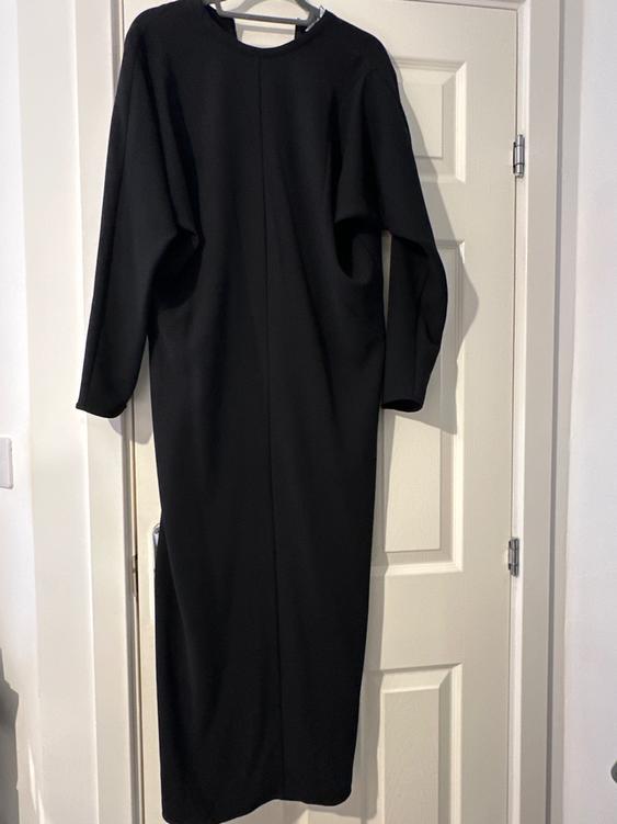 Long-sleeved black dress hanging on a white door. The design is simple and elegant, with a straight cut.