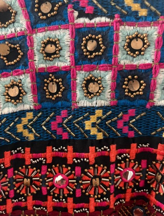 Close-up of a colourful fabric with geometric embroidery in blue, pink, red, and yellow, embellished with beads and metallic discs.