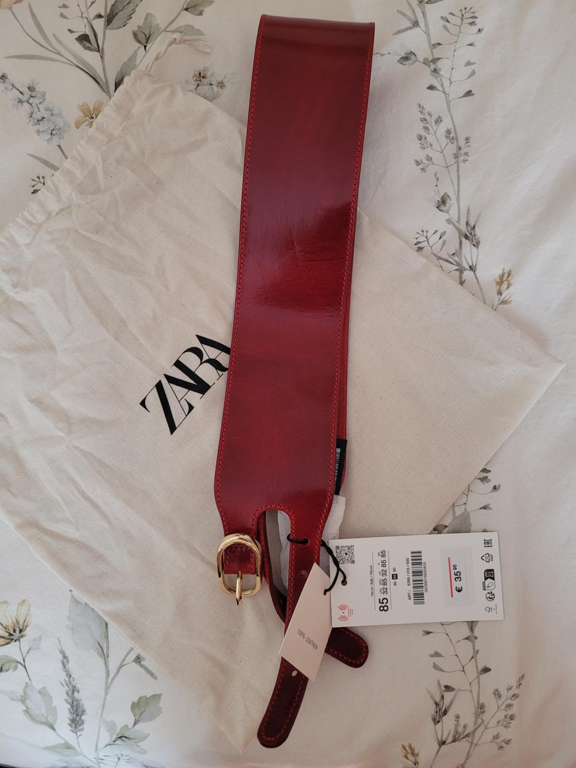 Red leather belt with a gold-coloured buckle on a fabric bag with the "ZARA" logo. Label shows price of £35.95.