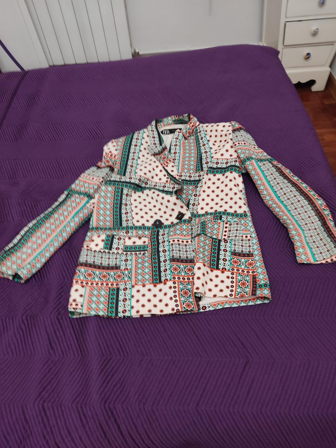 Multicoloured patterned jacket with geometric and floral designs on a bed with a purple bedspread in a room.