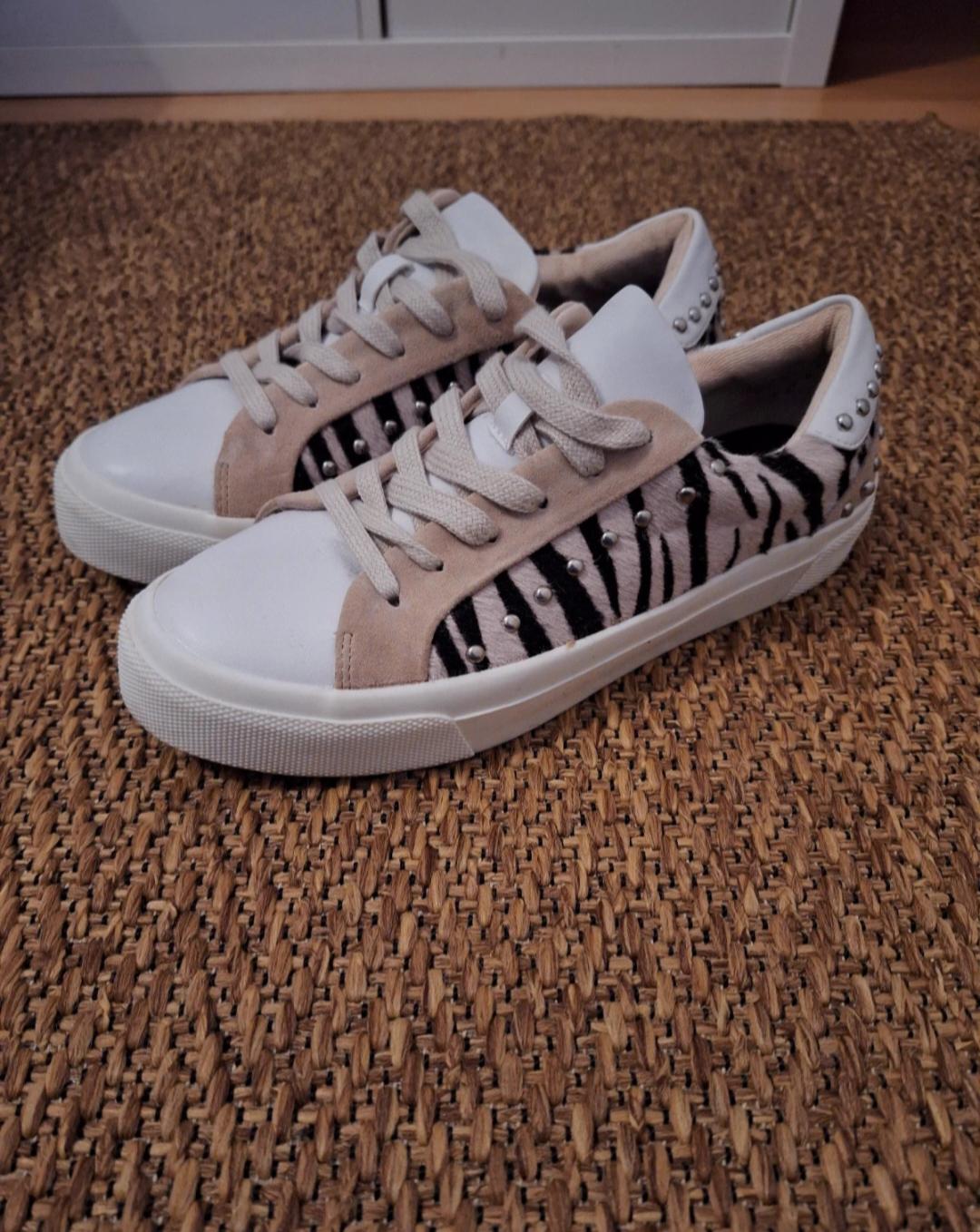 White trainers with animal print details and studs on the heel, on a natural fibre rug.