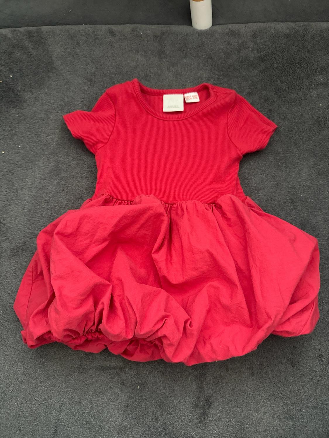 Red short-sleeve dress with a ribbed bodice and a bubble skirt against a gray background. Tag with text: KEEP AWAY FROM FIRE.