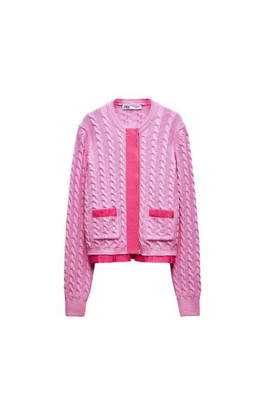 Pink cable-knit cardigan on a white background. Central band, pockets and pleated hem in deep pink. ZARA label at the neck.