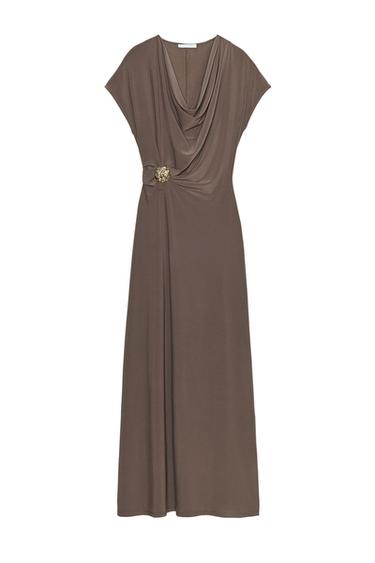 Front view of a draped brown dress with a flowing neckline, short sleeves and metal hardware detailing at the waist.