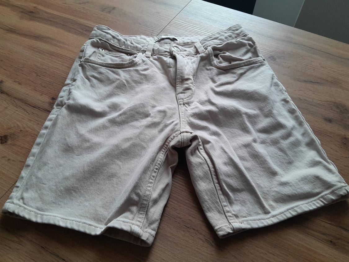 Beige cotton shorts on a wooden table, with front pockets and belt loops.