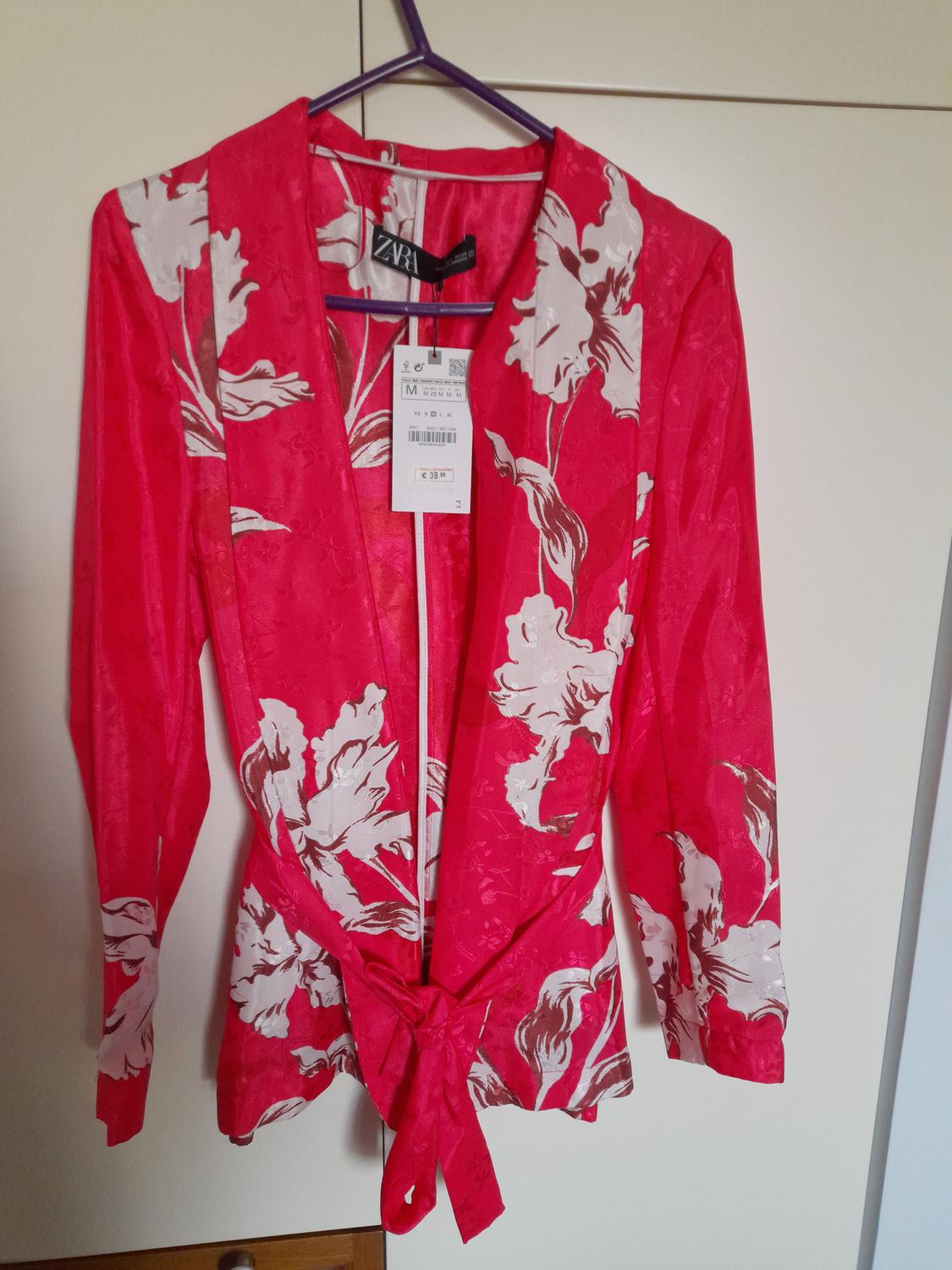 Red jacket with white floral print, hanging on a purple hanger. Visible tag with price of €39.99.