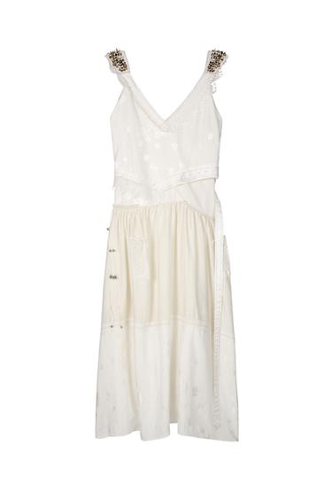 Front view of a white dress with decorated straps and side pockets.