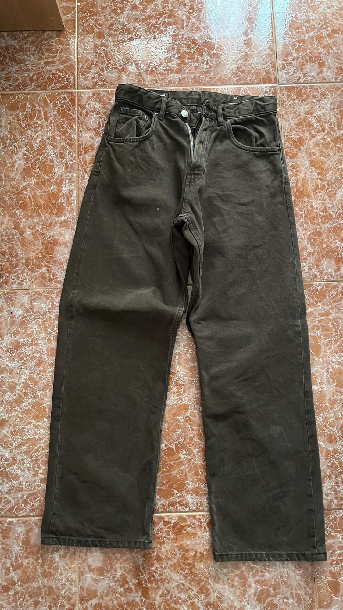 Dark, straight-leg trousers with pockets, laid out on a mottled brown tiled floor.
