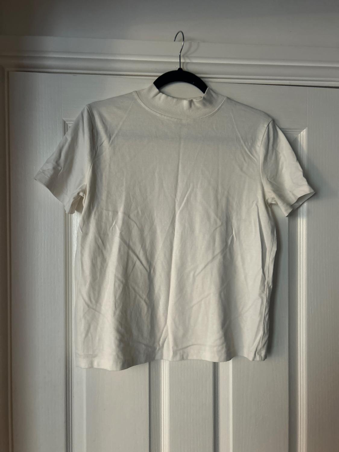 White short-sleeved t-shirt hanging on a black hanger over a white door. The fabric shows some creases.