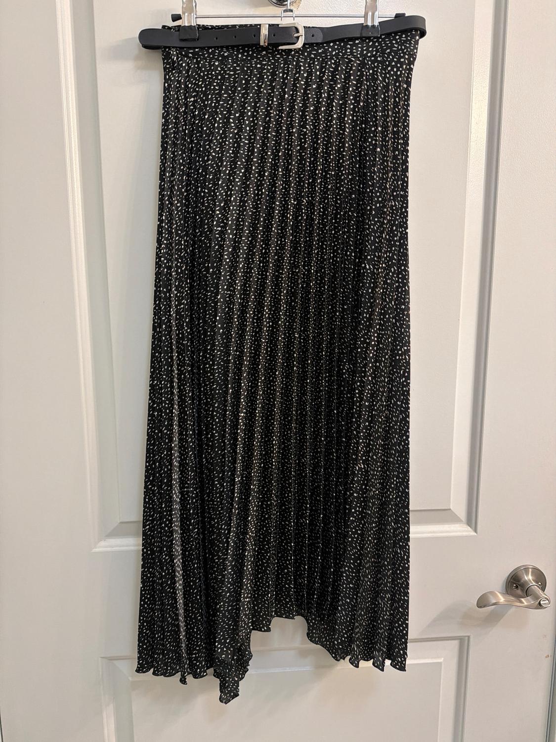 Black pleated skirt with white polka dot print hanging on a hanger over a white door.