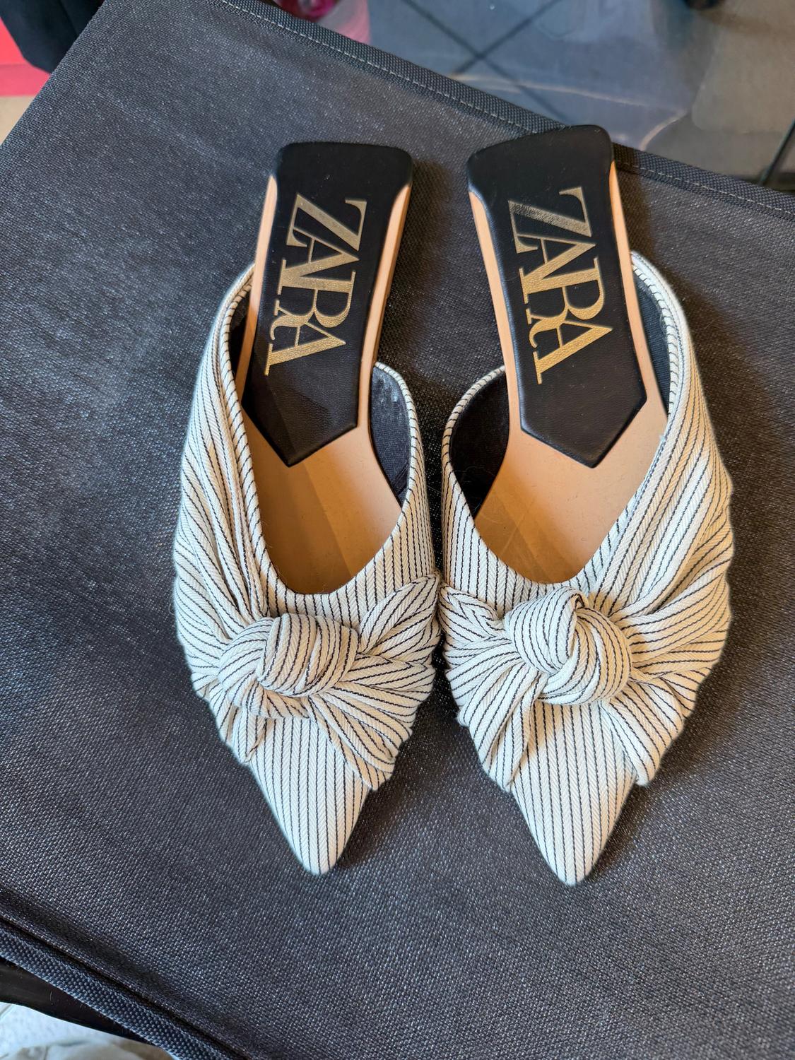 Backless high-heeled shoes with a knot and stripe design, on a dark surface. Insoles with the "ZARA" logo.