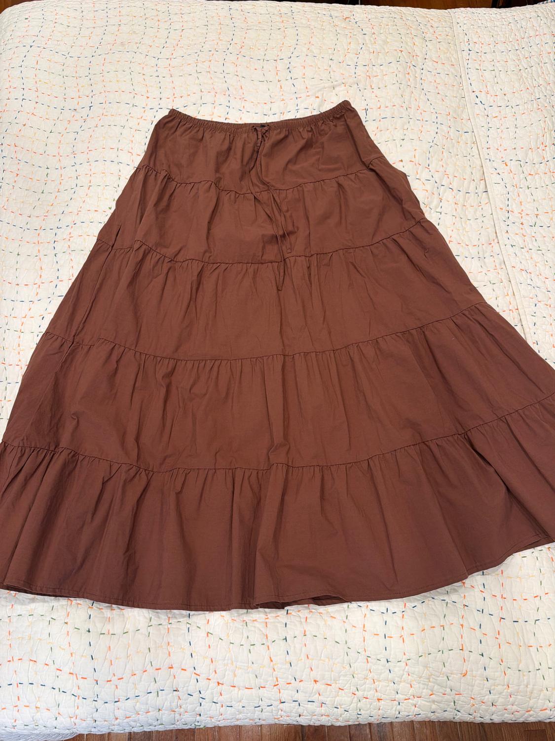 Brown tiered maxi skirt with an elastic waistband and drawstring, spread out on a white quilt with colorful stitching.