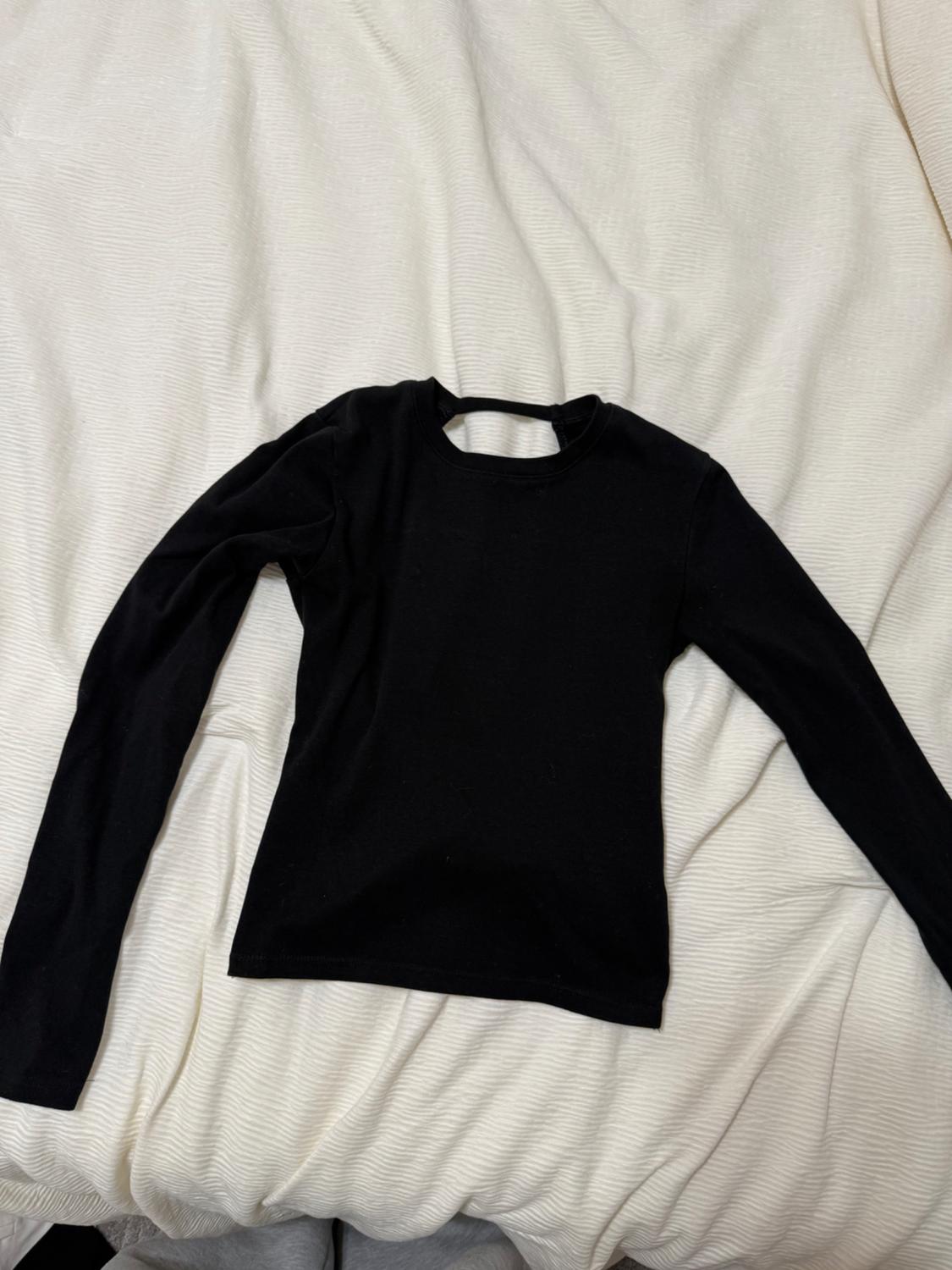 Black long-sleeved T-shirt on a bed with a crumpled white bedspread.