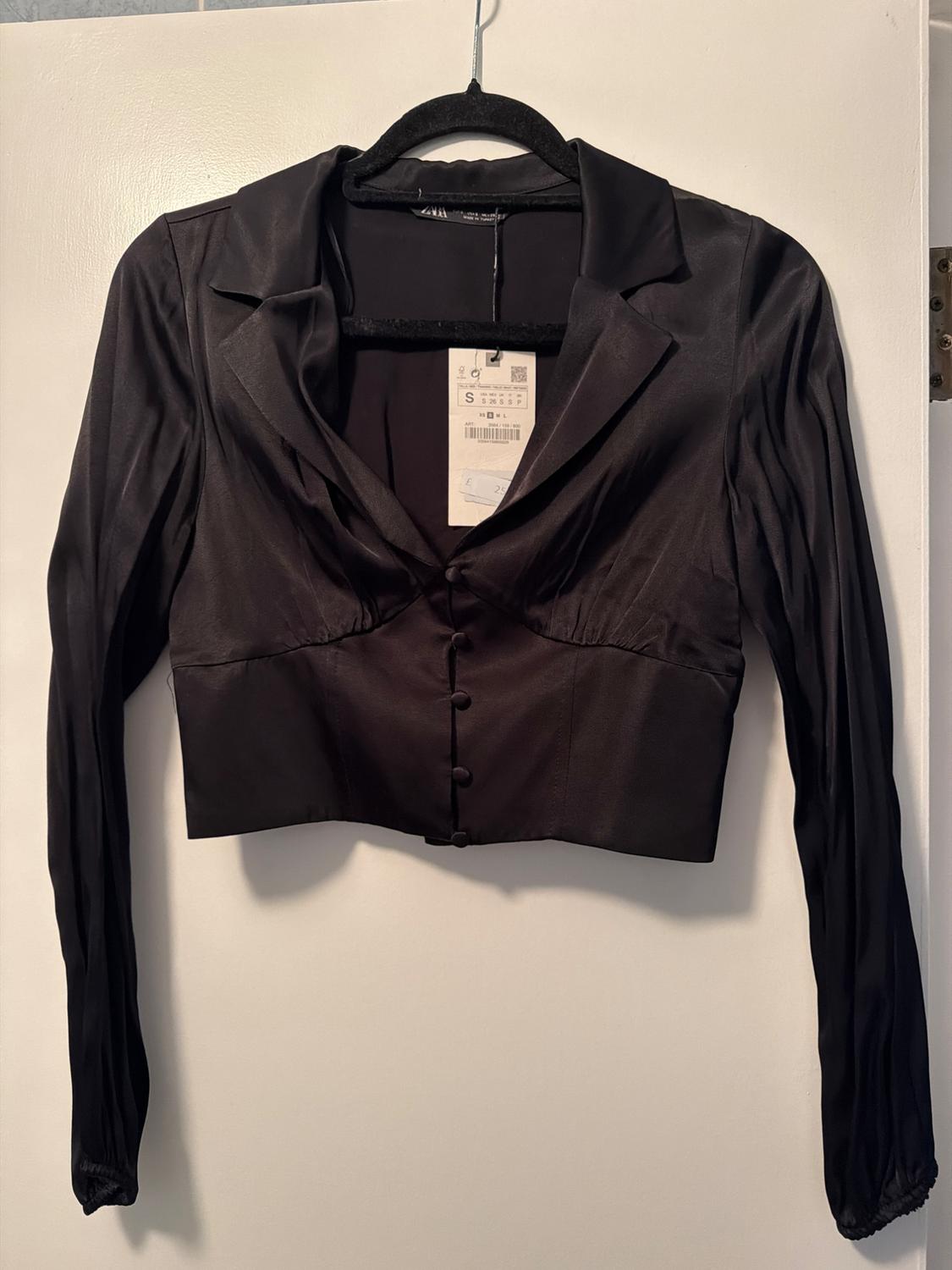 Black satin jacket with front buttons and long sleeves, hanging on a black hanger. Visible label with size S.