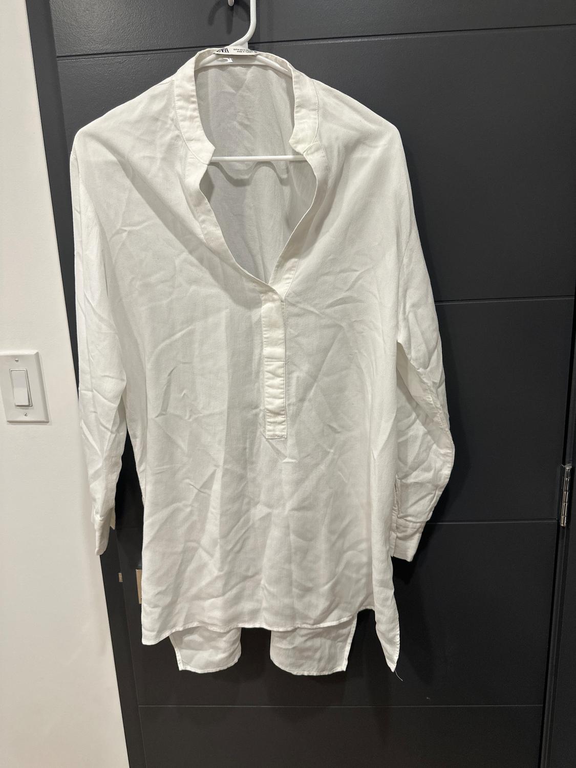 White long-sleeved shirt hanging on a hanger over a dark door. The fabric is wrinkled and has a simple design.
