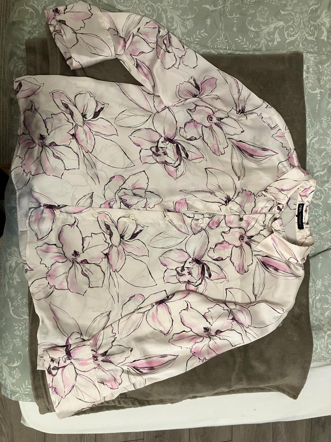 White long-sleeved shirt with a lilac and black floral print, laid out on a grey blanket and patterned bedsheets.