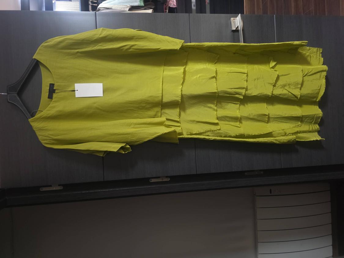 Short-sleeved lime green dress with a ruffled skirt, hanging on a hanger in front of a dark grey wardrobe.