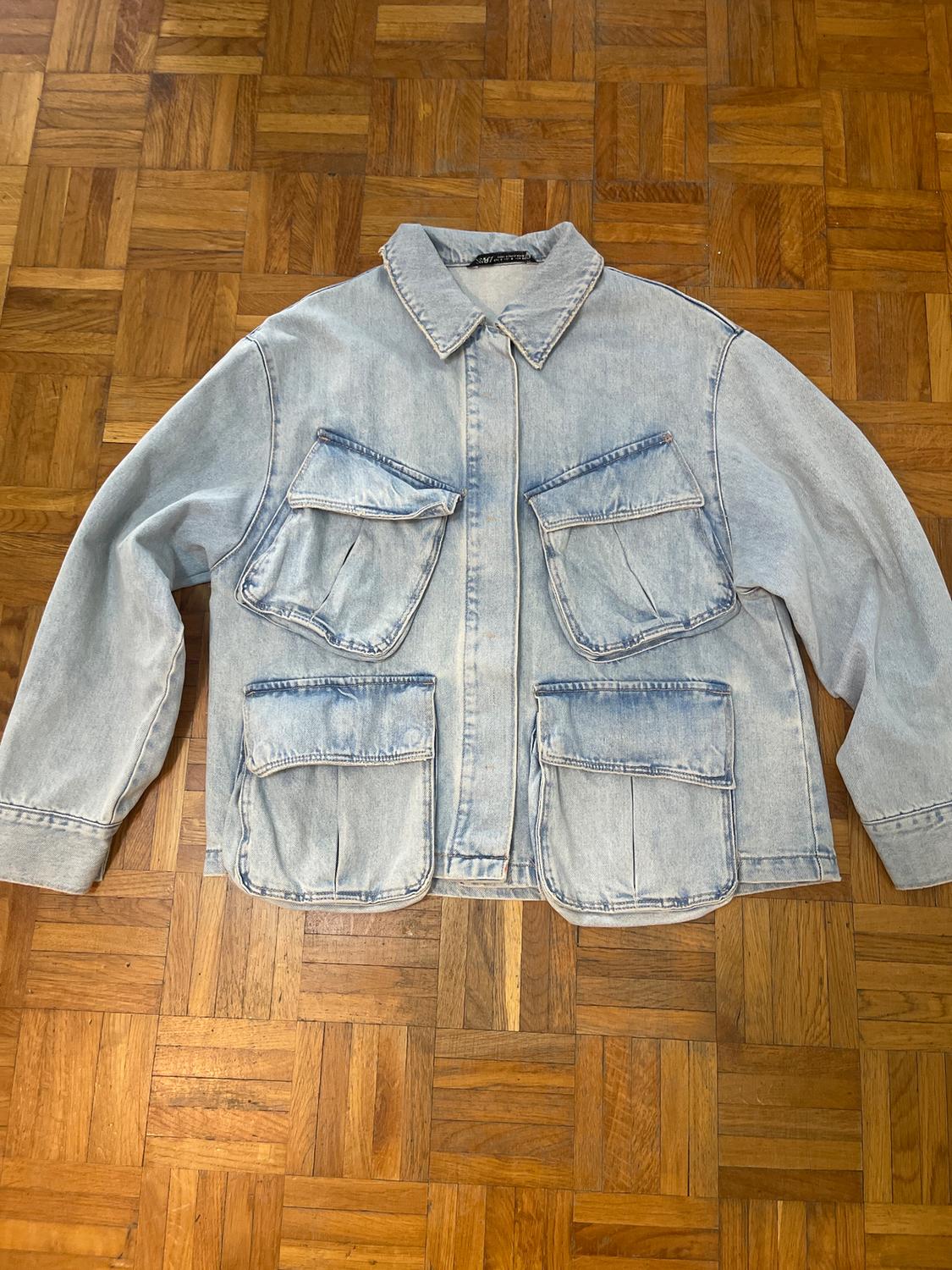 Light blue denim jacket with four large pockets on the front, on a wooden parquet floor.