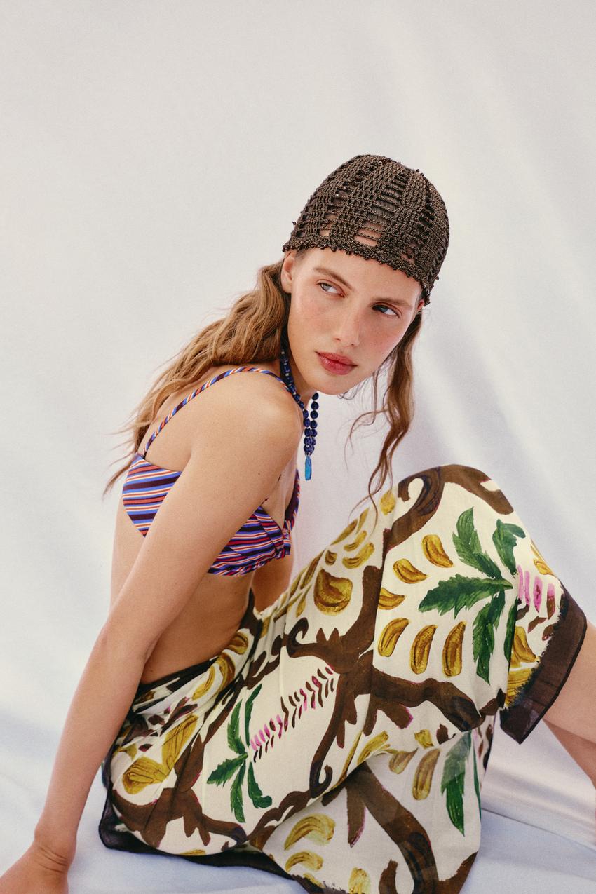 Brown openwork beanie set, striped bikini top, blue beaded necklace, and light skirt with a branch and leaf print.