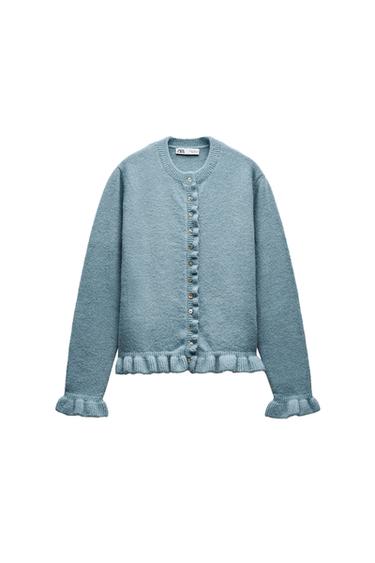 Front view of a blue cardigan with buttons and frill detailing on the cuffs and hem.