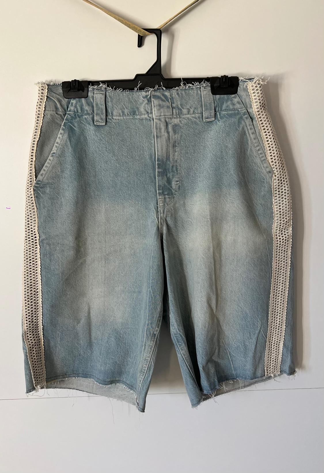 Light blue denim shorts with frayed edges and white lace detailing on the sides, hanging on a black hanger.
