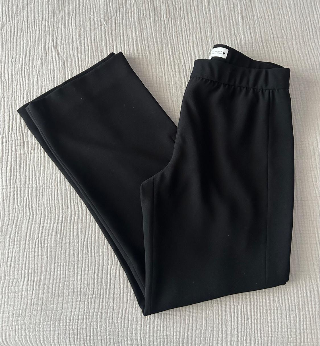 Black trousers made from soft fabric, folded on a textured white surface. Label visible at the waistband.