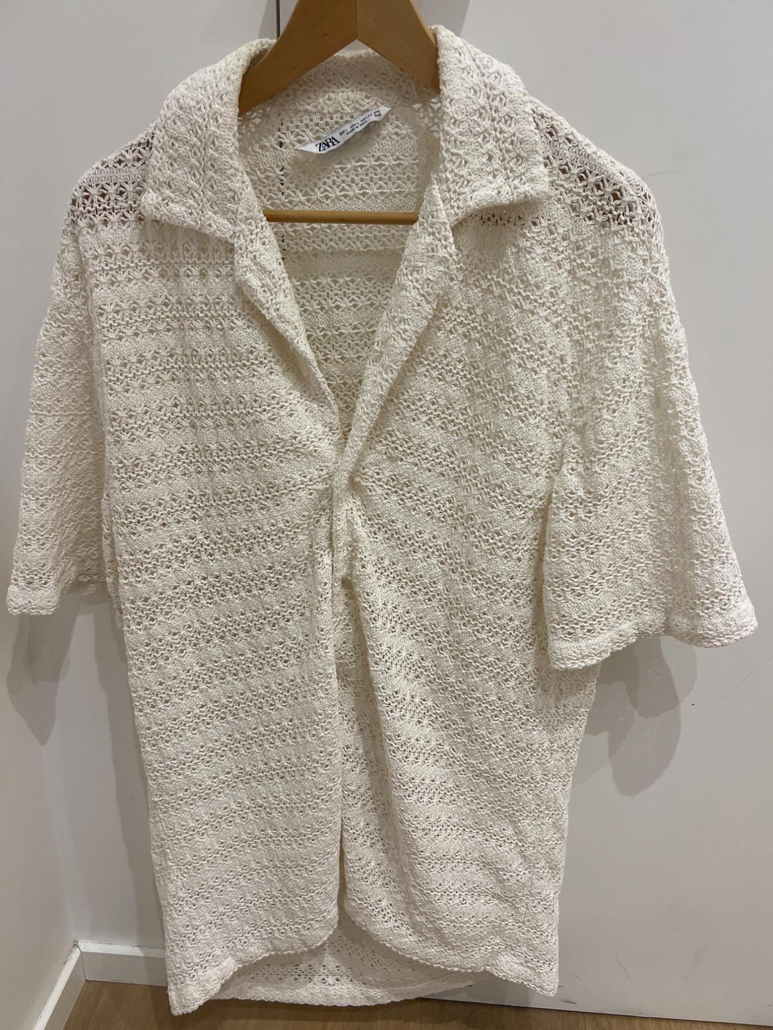 White lace shirt hanging on a wooden hanger, with visible Zara label, on a white background.