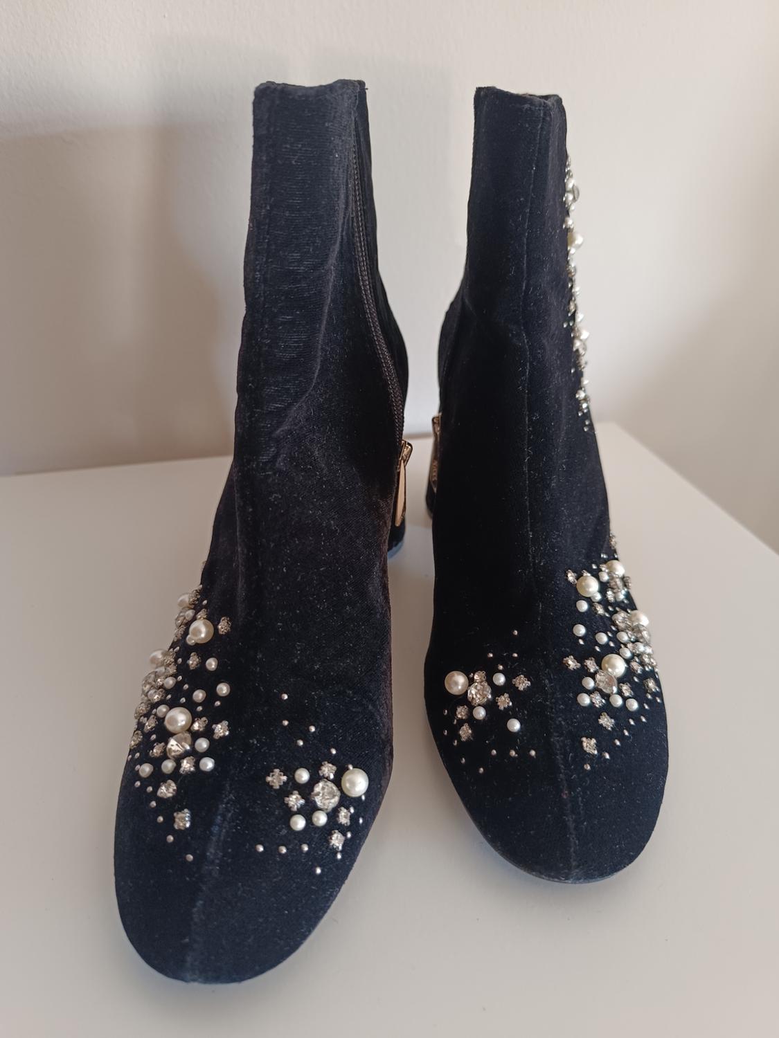 Black velvet ankle boots decorated with pearls and sparkly rhinestones, with a side zip, on a white background.
