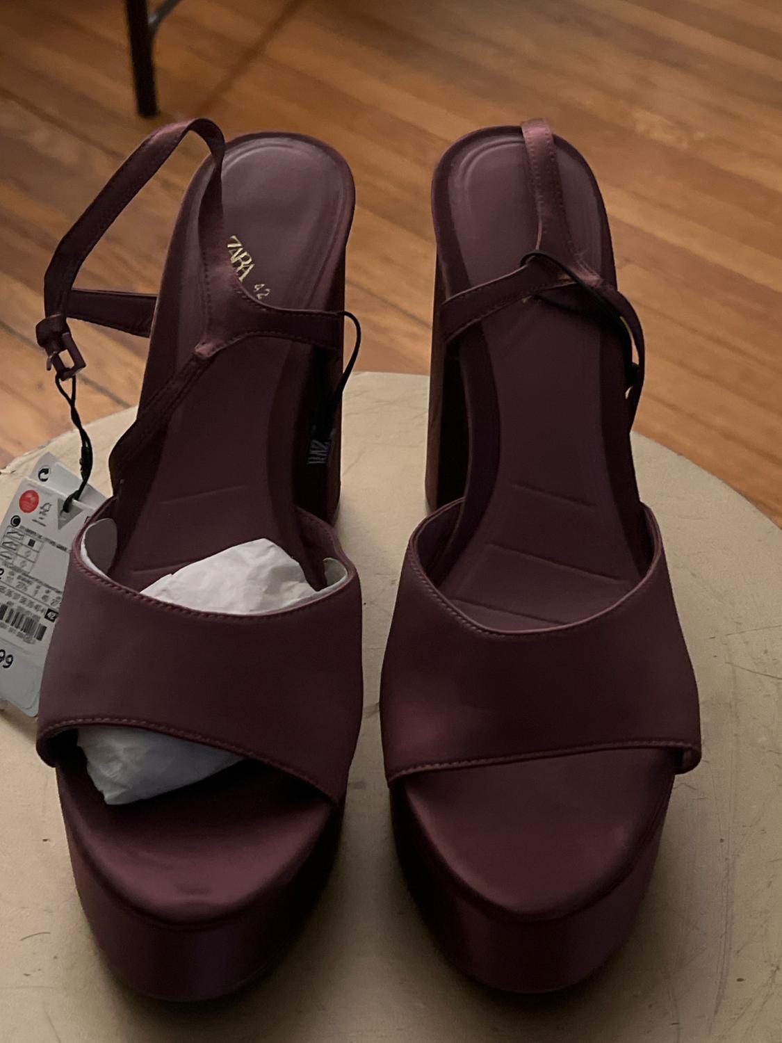 Burgundy platform sandals with crossover straps and a visible label, on a light wooden surface.