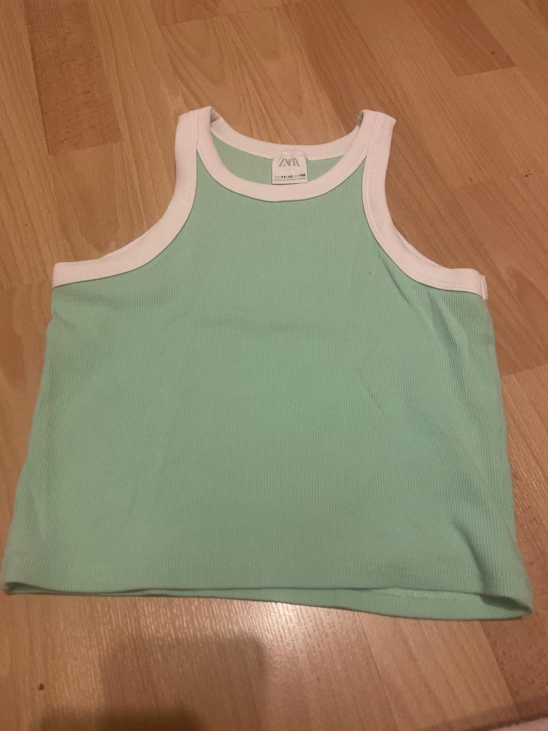 Mint green sleeveless top with white trim on a wooden floor. Visible label with text "ZARA".