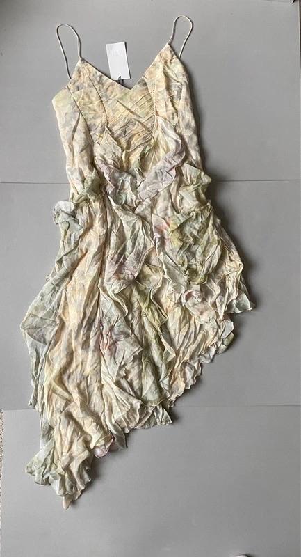 Asymmetric dress with spaghetti straps and a crinkled pastel print, on a grey background. White label visible at the top.