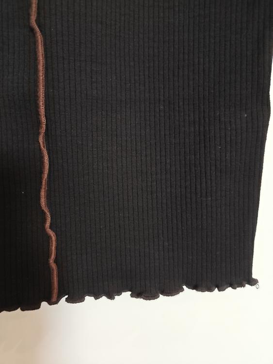 Black ribbed fabric with brown wavy stitching on the edge, on a white background.