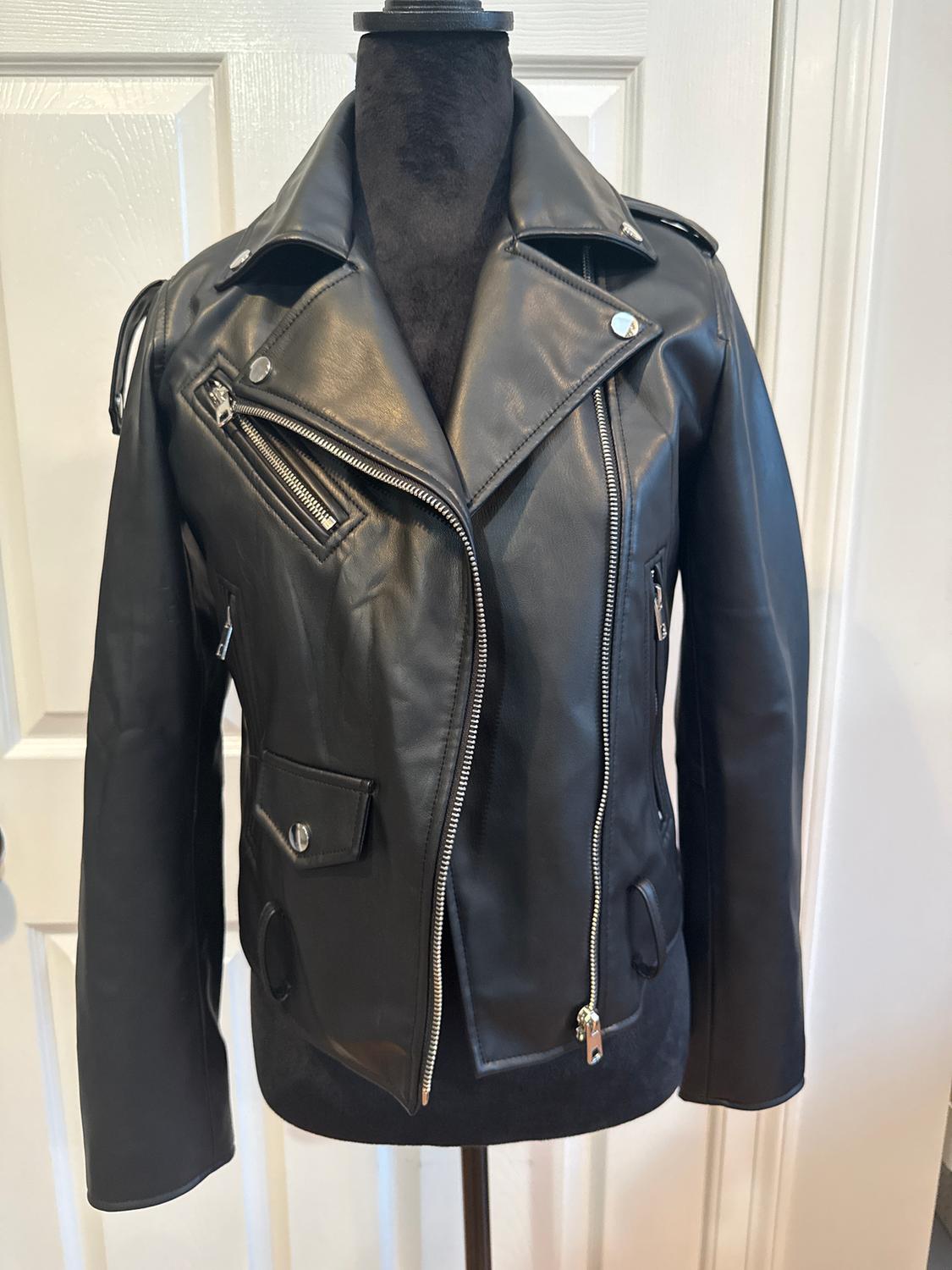 Black leather jacket with zips and lapels, displayed on a black mannequin in front of a white door.