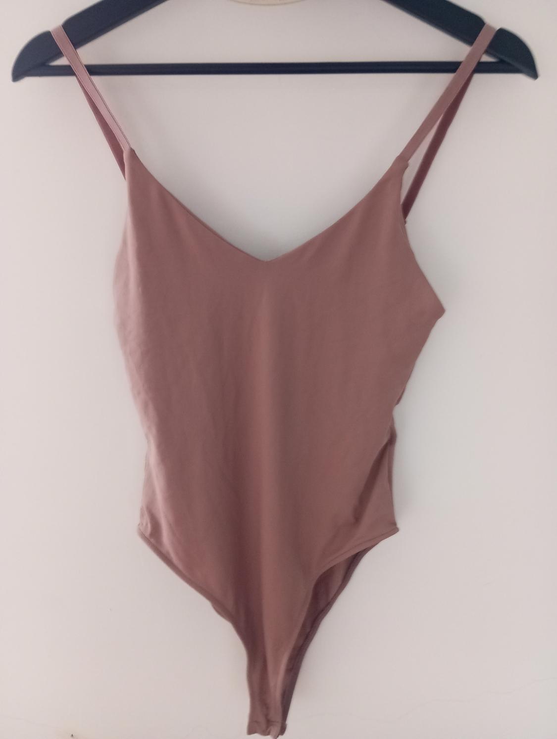 Light brown strappy bodysuit hanging on a black hanger against a white background.