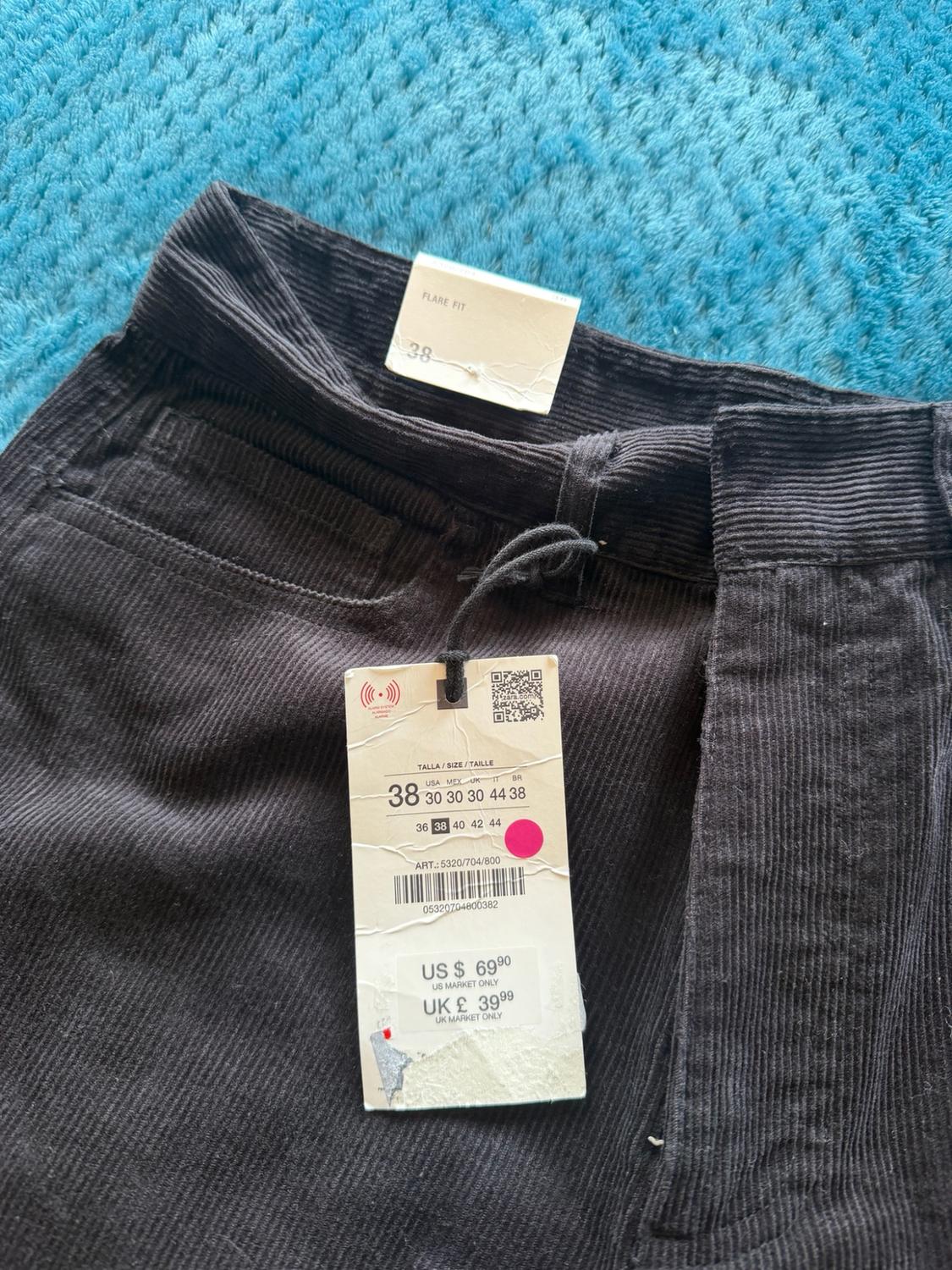 Black corduroy trousers on a blue background. Text labels: FLARE FIT 38, SIZE 38, ART.: 5320/704/800, US $ 69.90, UK £ 39.99.