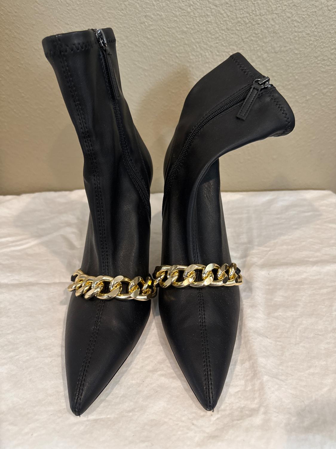 Front view of black heeled boots with a decorative gold chain.