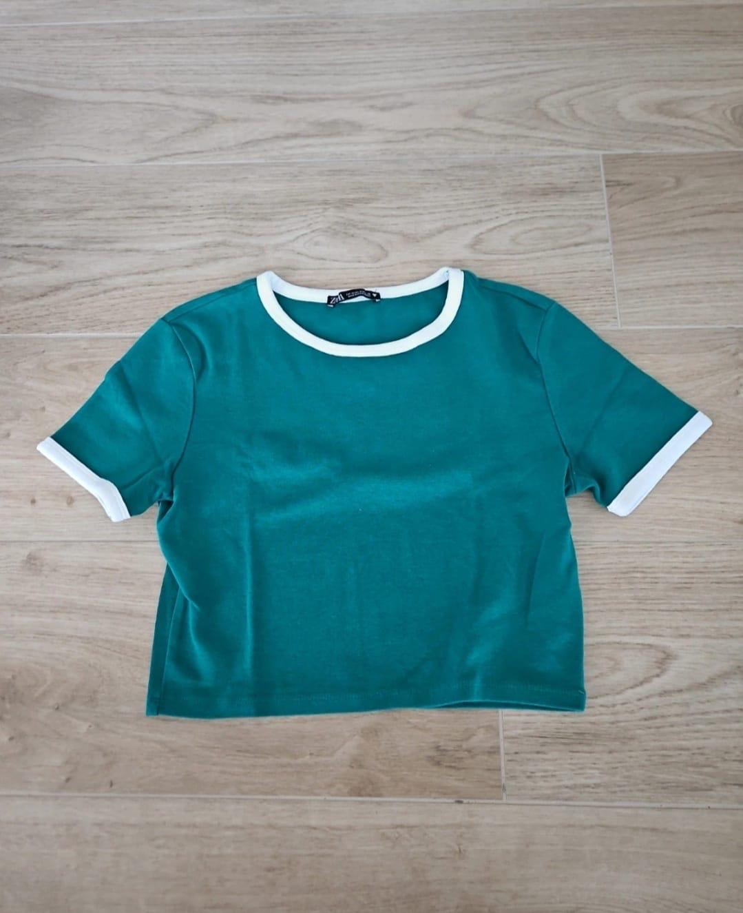 Green T-shirt with white trim on the collar and sleeves, on a light wooden floor.