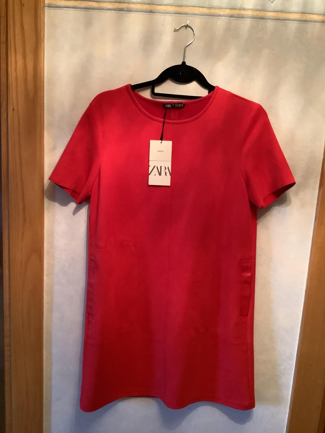 Short-sleeved red dress hanging on a black hanger, with a visible label that says "ZARA", against a light background.