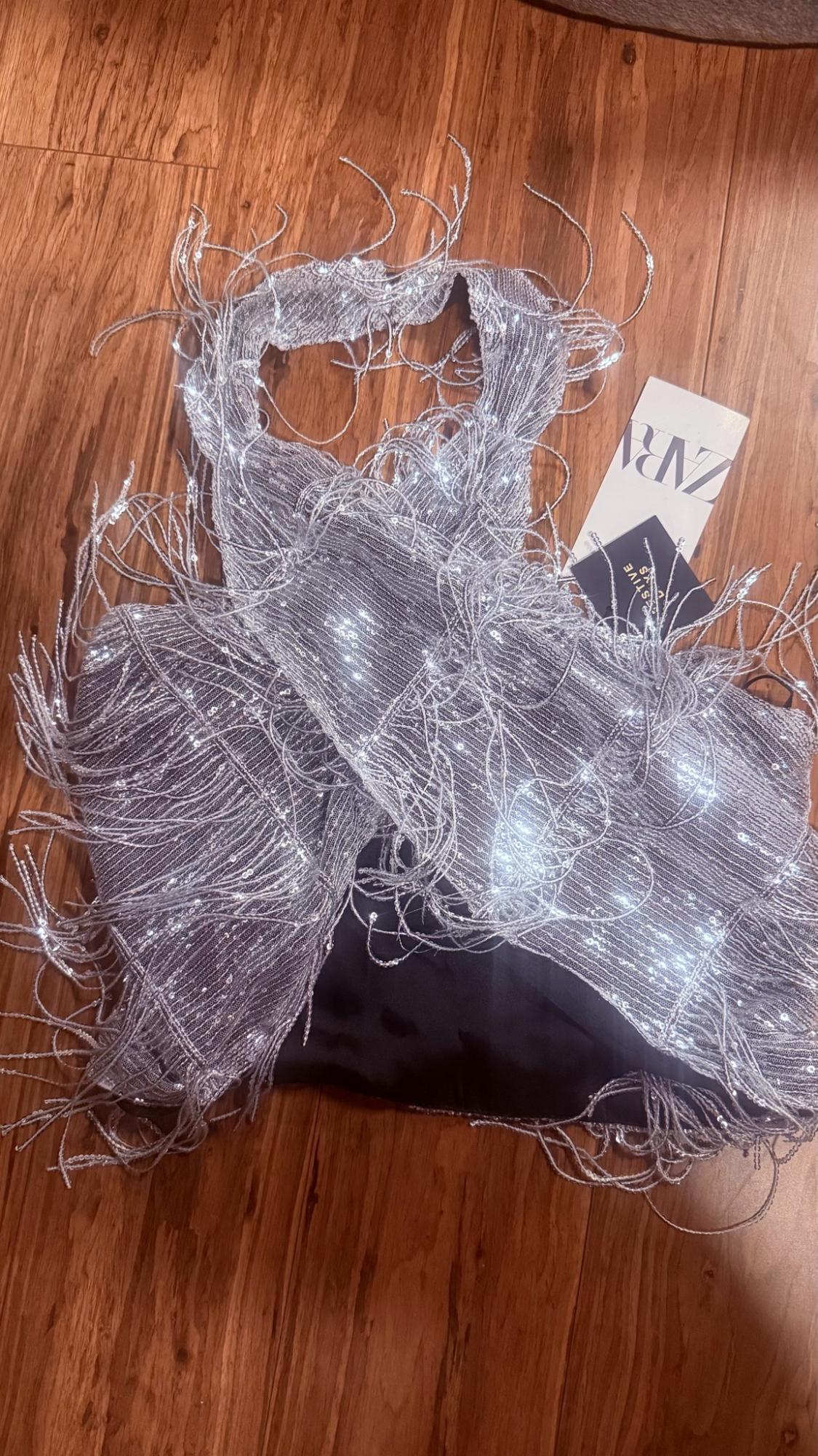 Silver sequined and fringed halter crop top on a wooden floor. Label with ZARA text.