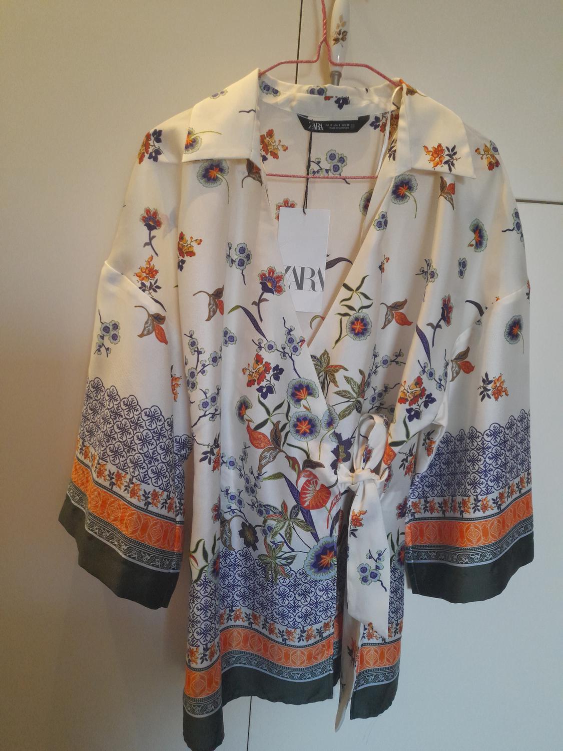 Blouse hanging with floral print in blue, orange, and green tones. Visible label with the text "ZARA". White background.