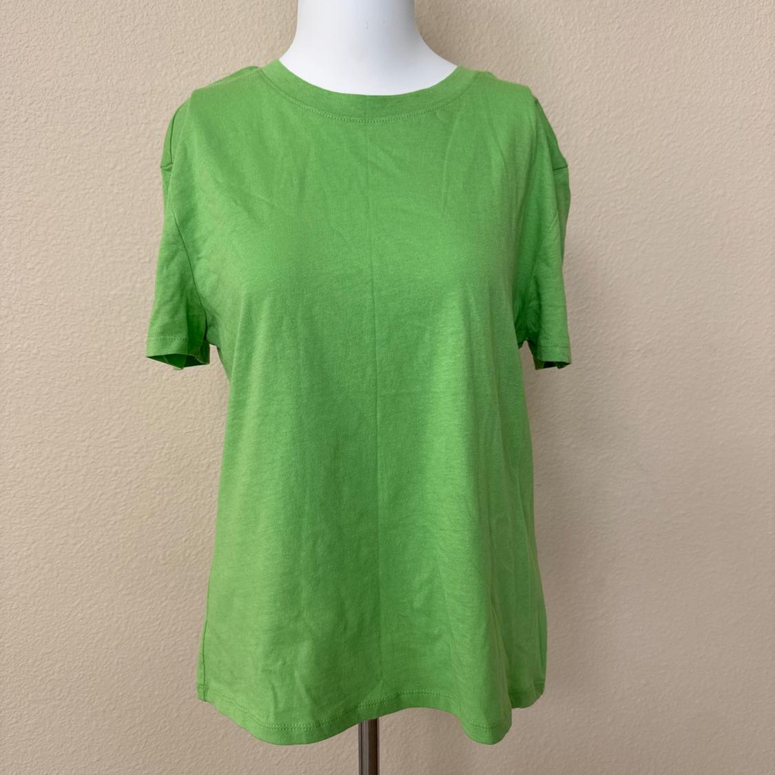 Short-sleeve basic t-shirt in bright green on a white mannequin. Textured beige wall background. Casual and relaxed style.