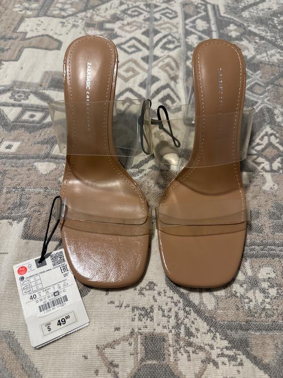 Brown high-heeled sandals with transparent straps on a patterned rug. Price tag: USD $49.90.